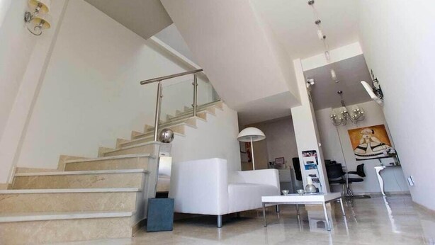 A modern interior with a staircase, a white sofa, a dining table, and a painting on the wall. - Hospedería Almundo (Tarifa)