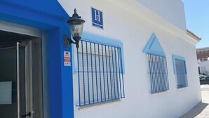 A building with a blue entrance, a sign with an 'H' and 'PLIVA', and barred windows. - Hospedería Almundo (Tarifa)