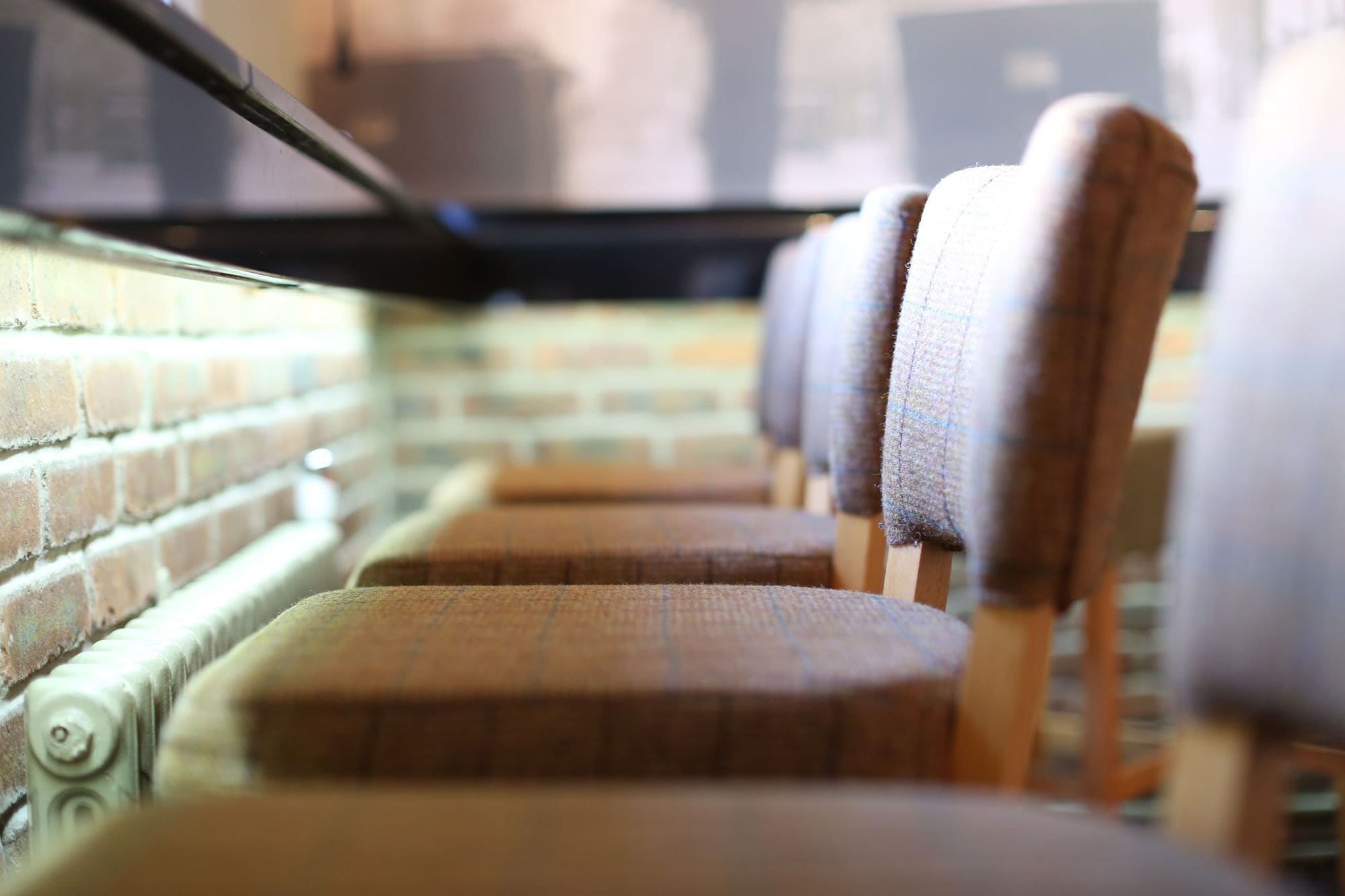 A row of wooden chairs with fabric seats and backs, arranged in a row against a brick wall.