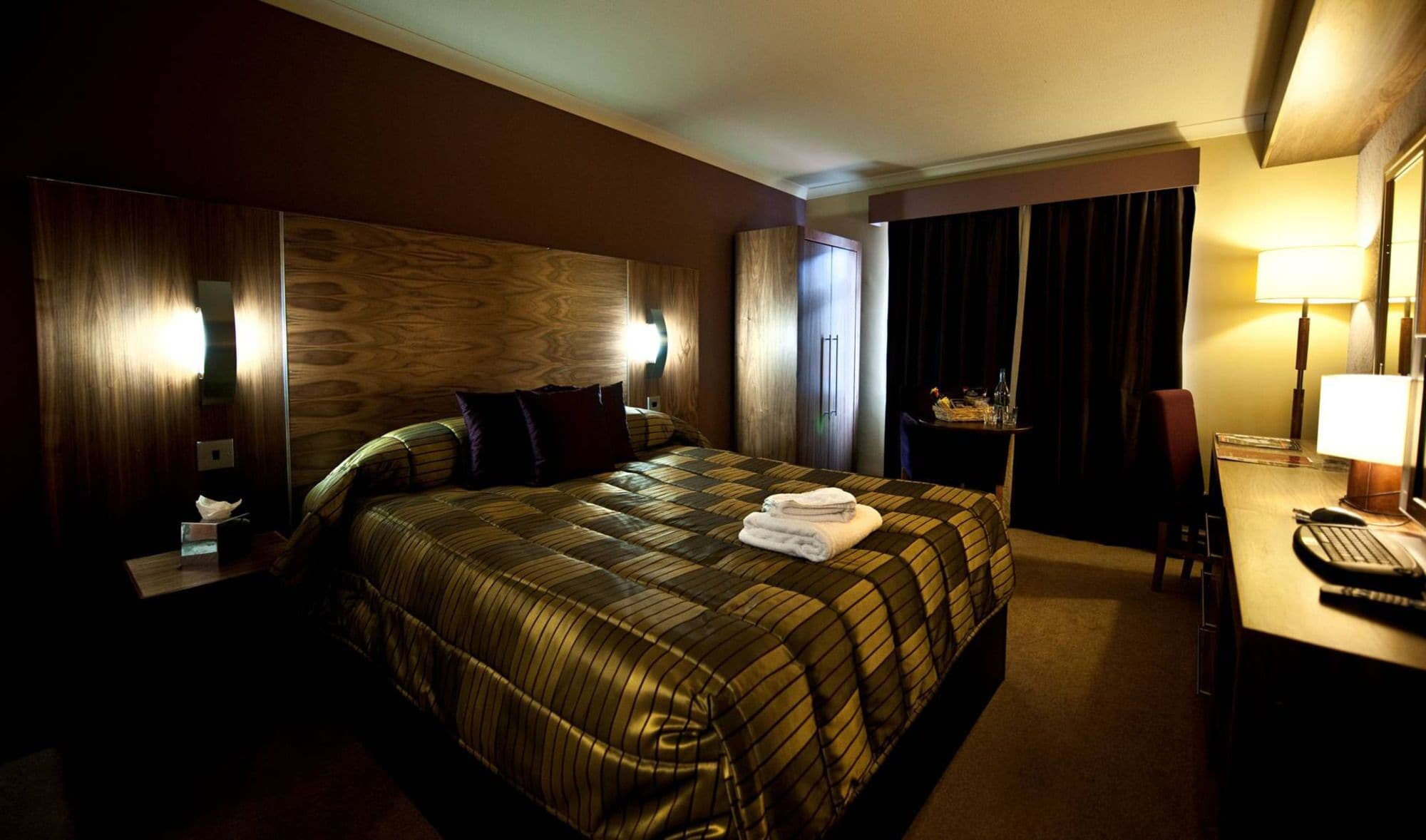 Una habitación de hotel con una cama grande, un escritorio con lámpara, una silla y una ventana con cortinas.