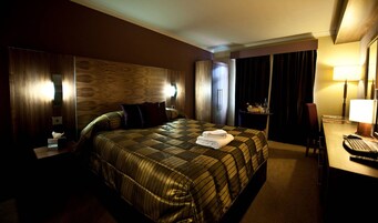 Una habitación de hotel con una cama grande, un escritorio con lámpara, una silla y una ventana con cortinas.