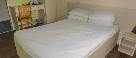 A bed with white bedding, a wooden chair, a desk with a coffee maker, and a small bedside table.