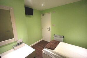 Une chambre avec un lit, une table de chevet blanche, un téléviseur fixé au mur et une porte.