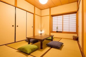 A traditional Japanese room with tatami flooring, a low table, cushions, sliding doors, and a window with shoji screens. - Hiroshima Danbara Guesthouse by Exseed (Hiroshima)