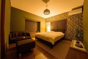 A bedroom with a bed, a sofa, a small table, and a decorative plant. - Hiroshima Danbara Guesthouse by Exseed (Hiroshima)