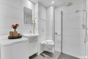 A modern bathroom with a white sink, mirror, and toilet, a shower area, and a vase with flowers on the counter. - Forenom Apartments Carl Berners Plass (Oslo)