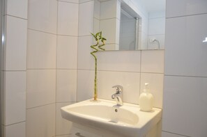 A bathroom with a white sink, a mirror, and a bamboo plant. - Forenom Apartments Carl Berners Plass (Oslo)