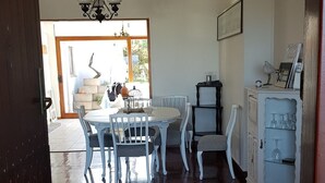 A dining area with a round table and chairs, a chandelier, and a cabinet with glassware. - Normandie On Sea (Hermanus)