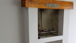 Una chimenea con un cartel de 'No Smoking' encima, una cesta de piñas y una pila de leña.