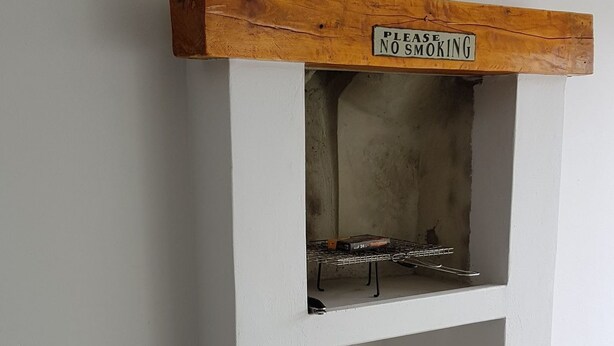 A fireplace with a 'No Smoking' sign above it, a basket of pinecones, and a stack of firewood. - Normandie On Sea (Hermanus)