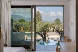A room with a bed, a table, and a view of a pool and landscape. - Tsamis Zante Suites (Zakynthos)