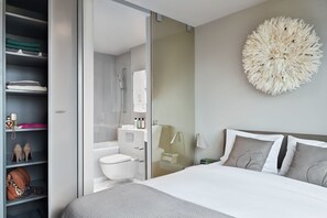 A modern bedroom with a large bed, a round decorative wall piece, a glass shower enclosure, and a wardrobe with folded clothes and shoes. - Visionapartments Frankfurt Gutleutstraße (Frankfurt)