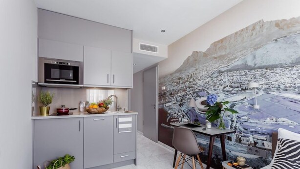 Una cocina moderna con armarios grises, horno empotrado y comedor con mesa y sillas.