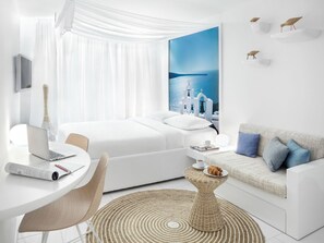 A modern hotel room with a bed, a desk, a laptop, a small round table with a croissant, and a view of a coastal scene with white buildings. - Visionapartments Frankfurt Gutleutstraße (Frankfurt)