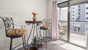Een balkon met een tafel en twee stoelen, een vaas met bloemen, en uitzicht op een gebouw.