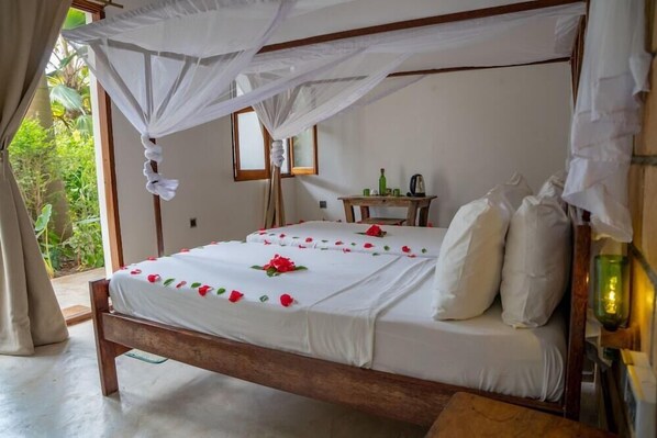 A bed with a canopy, white bedding, and red flowers. - Aluna Beach Lodge (Nungwi)