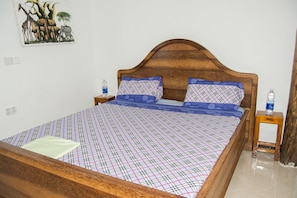 A neatly made bed with a plaid bedspread, two matching pillows, and a wooden headboard. There is a small bedside table with a water bottle on it. - Aluna Beach Lodge (Nungwi)