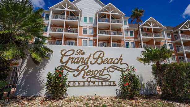 A sign for The Grand Beach Resort Condominium with a multi-story building and balconies. - The East Beach Classic | Ground Floor Convenience (Gulf Shores)
