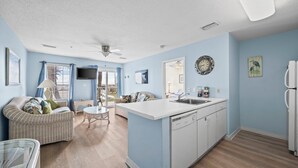 A compact living space with a kitchenette, a dining area with a table and chairs, a sofa, and a ceiling fan. - The East Beach Classic | Ground Floor Convenience (Gulf Shores)
