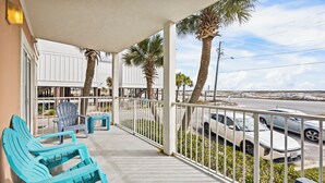 A covered outdoor area with turquoise chairs, a small table, and a view of a road with cars. - The East Beach Classic | Ground Floor Convenience (Gulf Shores)