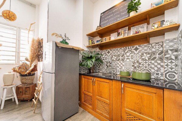 A kitchen with patterned backsplash, wooden cabinets, a refrigerator, and a shelf with books and decorative items. - Saigon Cactus Homestay (Ho Chi Minh City)