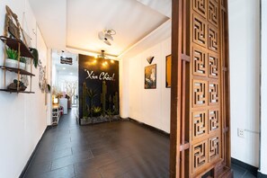 Un passadís amb terra de rajola fosca, un panell decoratiu de fusta i un senyal que diu 'Xin Chao!'.