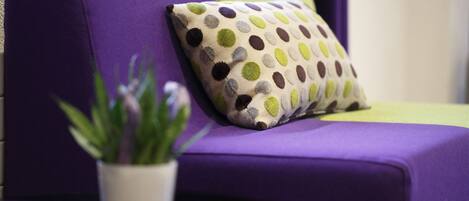 Un sofá morado con un cojín de lunares y una pequeña planta en maceta.
