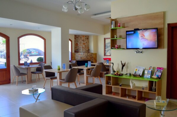 A modern hotel lobby with a stone fireplace, comfortable seating, a flat-screen TV, and a reception desk with informational brochures.