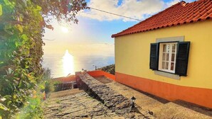A yellow building with a red-tiled roof and a stone staircase leading to a window with black shutters. - Quinta São Lourenço - Casa Frente | Sunset - Pool - Seaview (FAJÃ DA OVELHA)