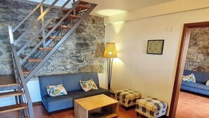 A room with a stone wall, a blue sofa, a wooden coffee table, a lamp, and a staircase. - Quinta São Lourenço - Casa Frente | Sunset - Pool - Seaview (FAJÃ DA OVELHA)