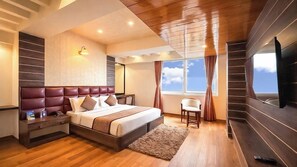 A modern bedroom with a large bed, bedside tables, a TV, and a window with curtains. - Jai Hotels (Darjeeling)