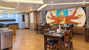 Um restaurante com mesas e cadeiras de madeira, um grande mural na parede e uma área de cozinha ao fundo.