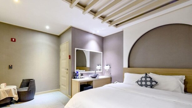 A hotel room with a bed, bedside table, and a desk with a mirror. - 1 Night 2 Days Hotel (Yangsan)