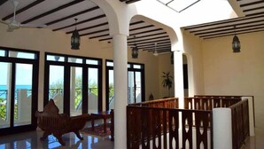 A spacious interior with a high ceiling, large windows, and a balcony with a view. - Villa Serenity (Jambiani)