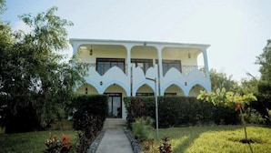 A two-story building with a central entrance, surrounded by a garden with a pathway leading to the door. - Villa Serenity (Jambiani)