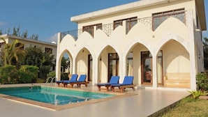 A hotel with a swimming pool, blue lounge chairs, and a white facade with arches. - Villa Serenity (Jambiani)