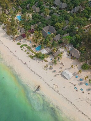An aerial view of a beach resort with multiple bungalow-style accommodations, a swimming pool, and a sandy beach. - Sharazad Villa (Jambiani)