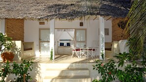 A covered outdoor seating area with a table and chairs, surrounded by potted plants and a staircase leading up. - Sharazad Villa (Jambiani)