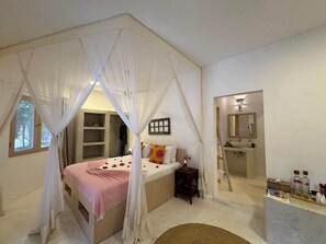 Camera da letto con letto a baldacchino, un comodino, uno specchio e bagno con lavandino e articoli da toilette.