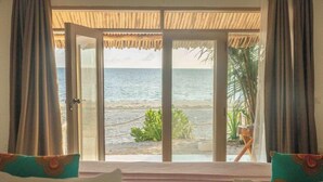 A room with a view of the sea, a bed with pillows, and a plant near the window. - Sharazad Villa (Jambiani)