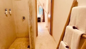 A bathroom with a shower, a towel rack, and a door leading to another room. - Sharazad Villa (Jambiani)