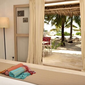 Ein Zimmer mit Blick auf einen Strand, ein Stuhl, eine Lampe und ein Bett mit Decke.