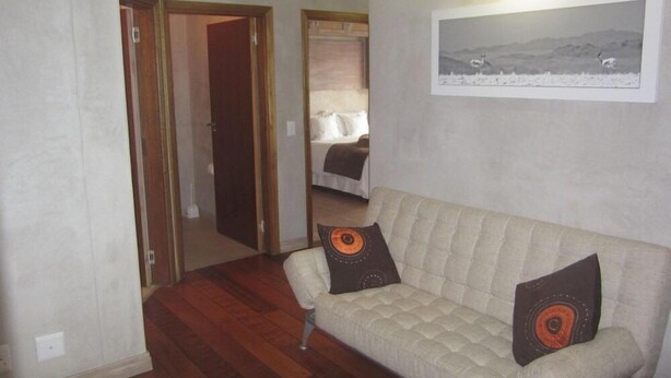 A living room with a beige sofa, two decorative pillows, a framed picture on the wall, and a wooden floor. - Atlantik Sicht Sef Catering Apartment Self Catering (Swakopmund)