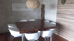 A dining area with a wooden table and white chairs, a hanging light fixture, and a wall-mounted switch. - Atlantik Sicht Sef Catering Apartment Self Catering (Swakopmund)