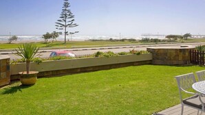 A patio with a view of the ocean, a tall tree, and a red car on the road. - Atlantik Sicht Sef Catering Apartment Self Catering (Swakopmund)