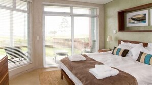 A hotel room with a large bed, a bedside table, a lamp, and a view through the window. - Atlantik Sicht Sef Catering Apartment Self Catering (Swakopmund)