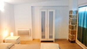 A bedroom with a bed, a nightstand, a wardrobe, and a stone wall. - F3 Hostels (Cascais)