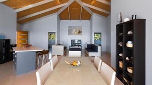 Ein geräumiger Wohnbereich mit hoher Decke, einem Esstisch mit Stühlen, einer Küchenzeile und einer Sitzecke mit Sofa und Fernseher.