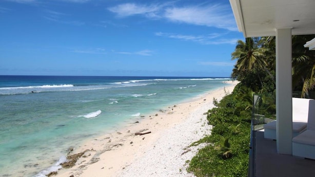 Blick auf einen Strand vom Balkon aus, mit blauem Himmel und Meereswellen.