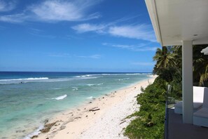 Blick auf einen Strand vom Balkon aus, mit blauem Himmel und Meereswellen.